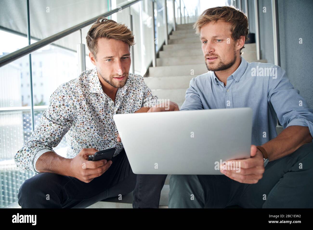 Two young businessmen sitting on stairs using laptop Stock Photo