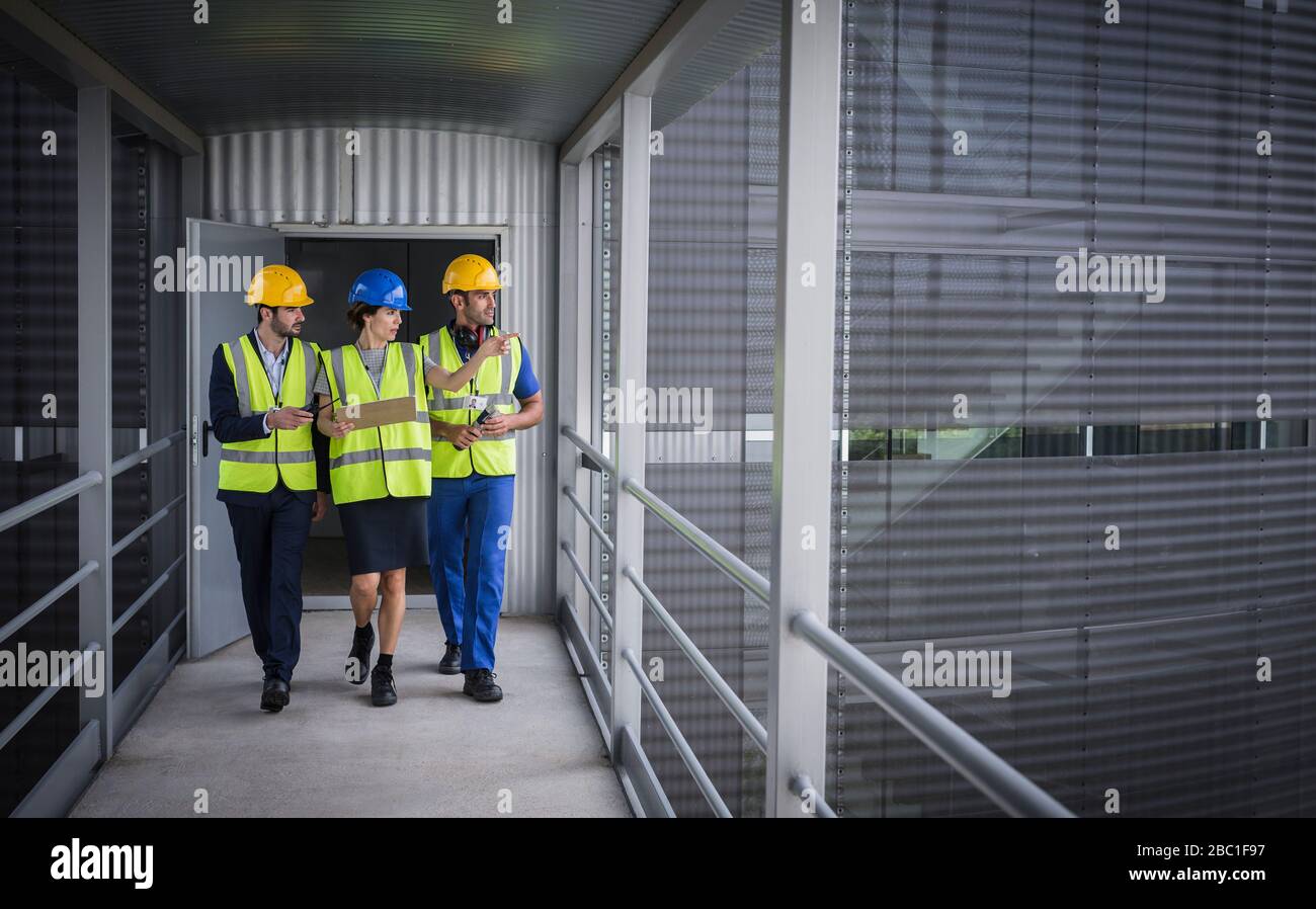 Supervisors with clipboard walking and talking on elevated walkway outside factory Stock Photo
