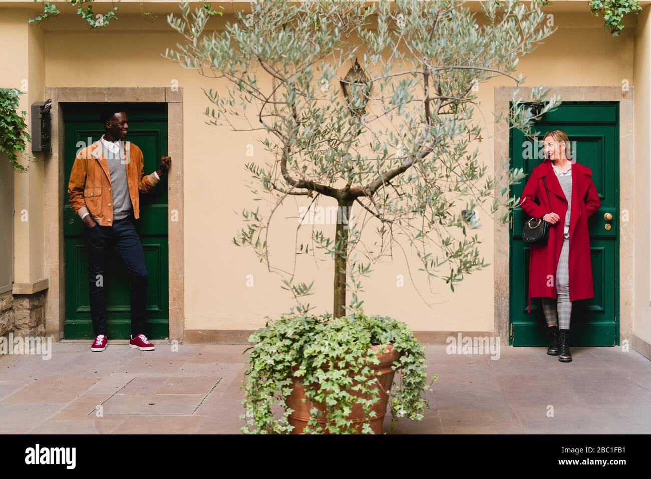 Smiling young man and woman standing at front doors in patio looking at each other Stock Photo