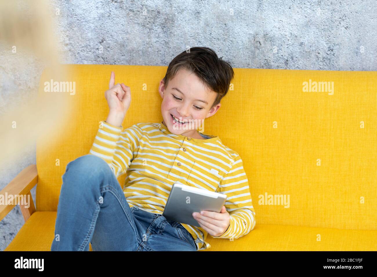 Boy playing with tablet on yellow couch Stock Photo