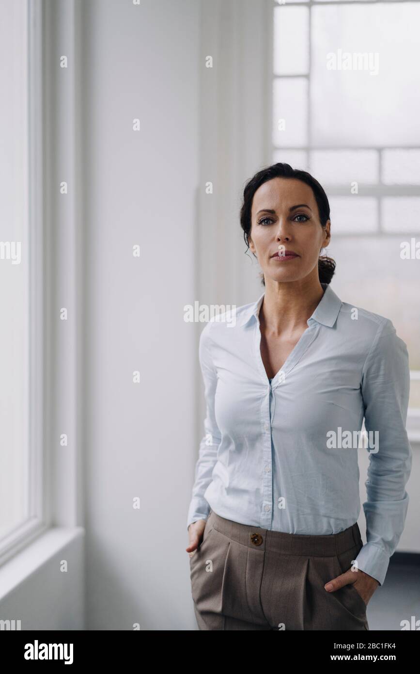 Successful businesswoman, standing by window, with hands in pockets Stock Photo