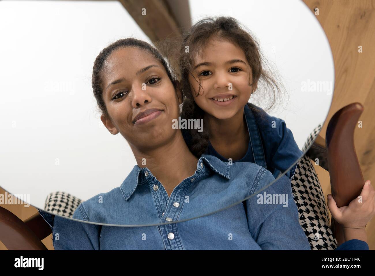 Mirror image of smiling mother and her happy little daughter Stock Photo