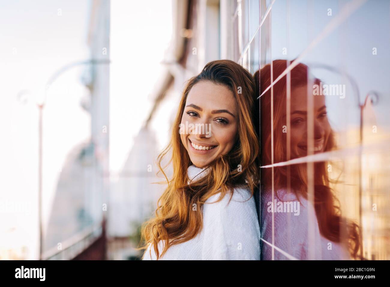 Portrait of happy young woman leaning against a tile wall Stock Photo