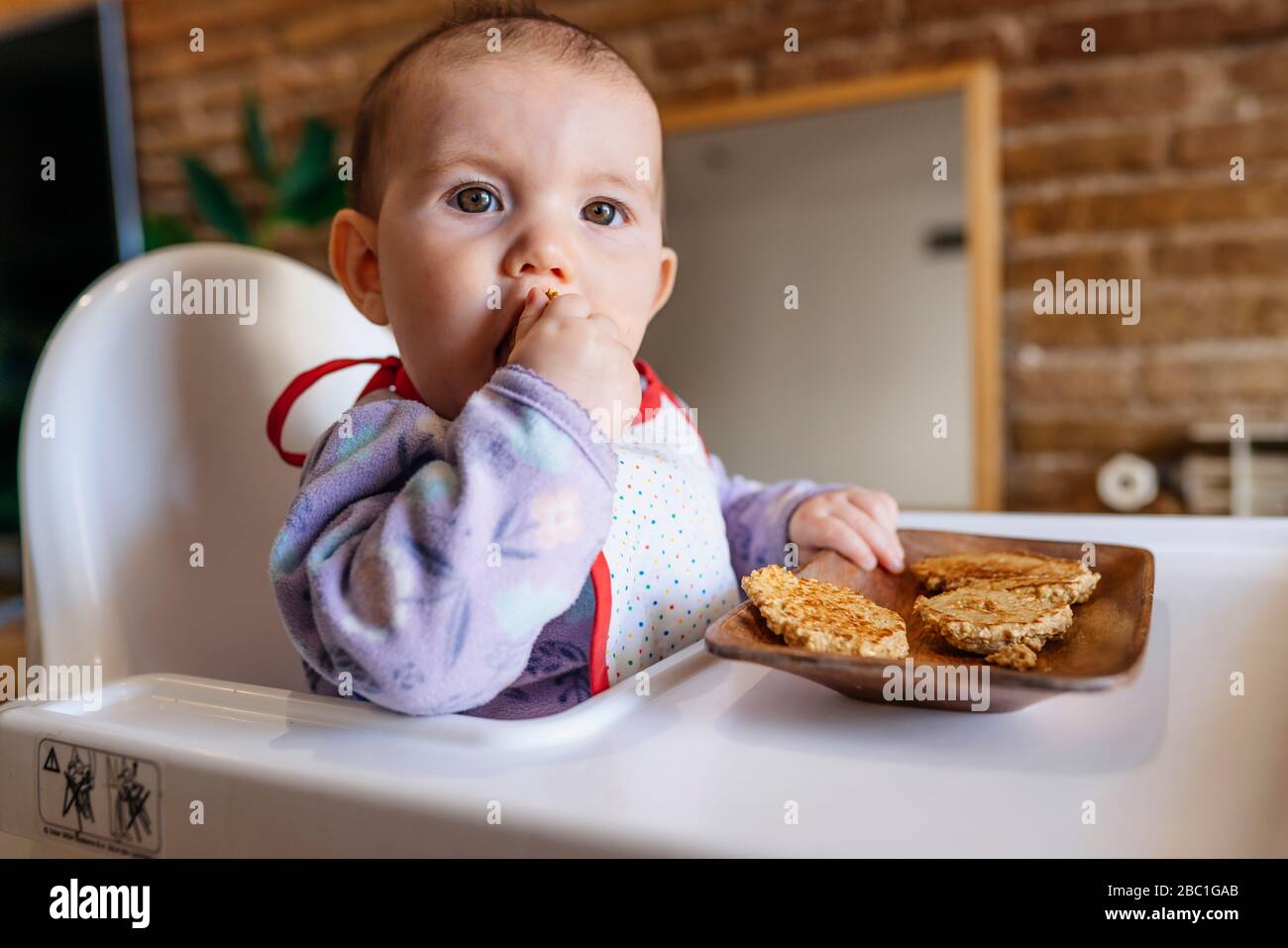 Portrait of baby girl sitting in high chair eating homemade oatmeal