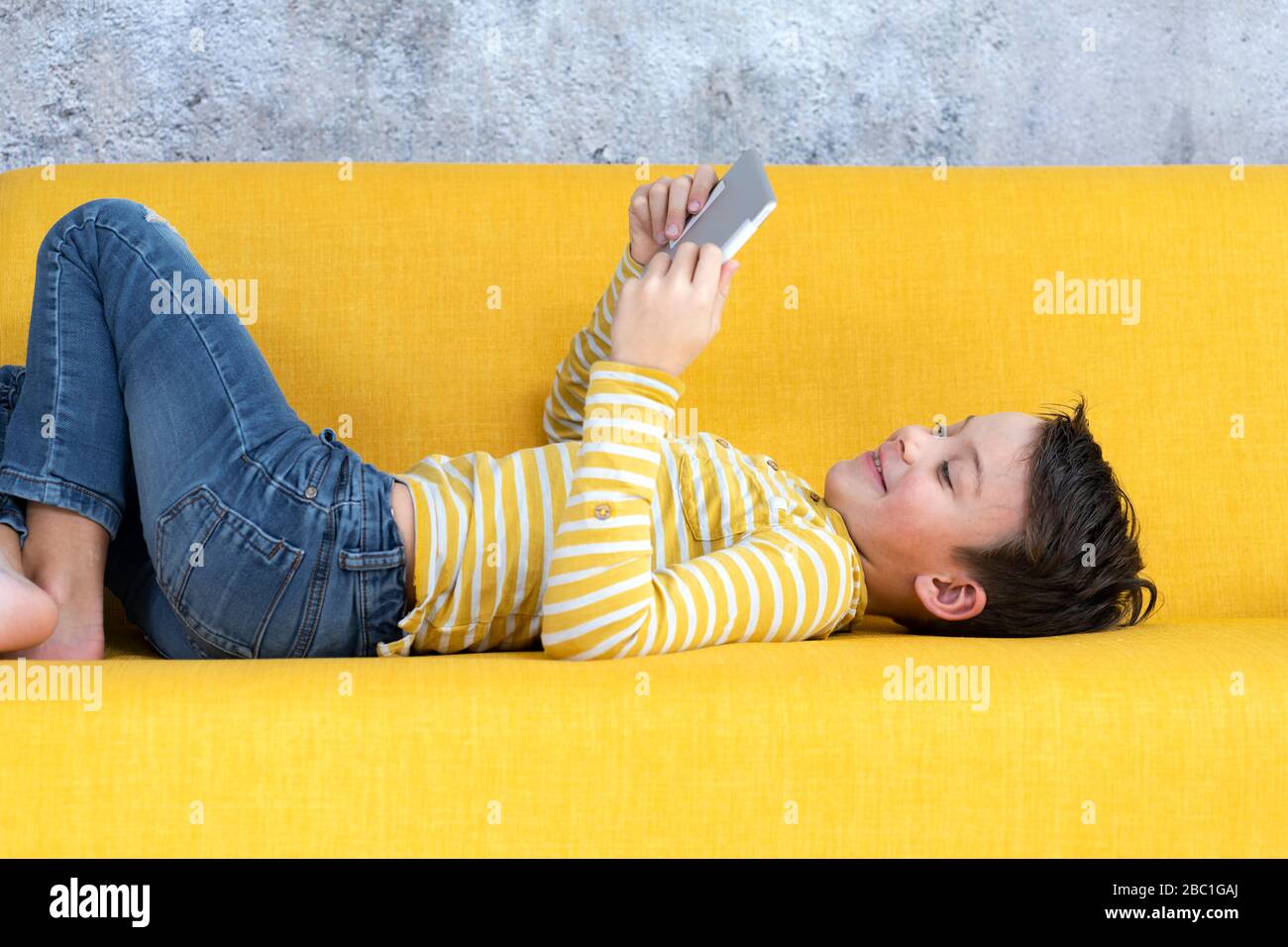 Boy playing with tablet on yellow couch Stock Photo