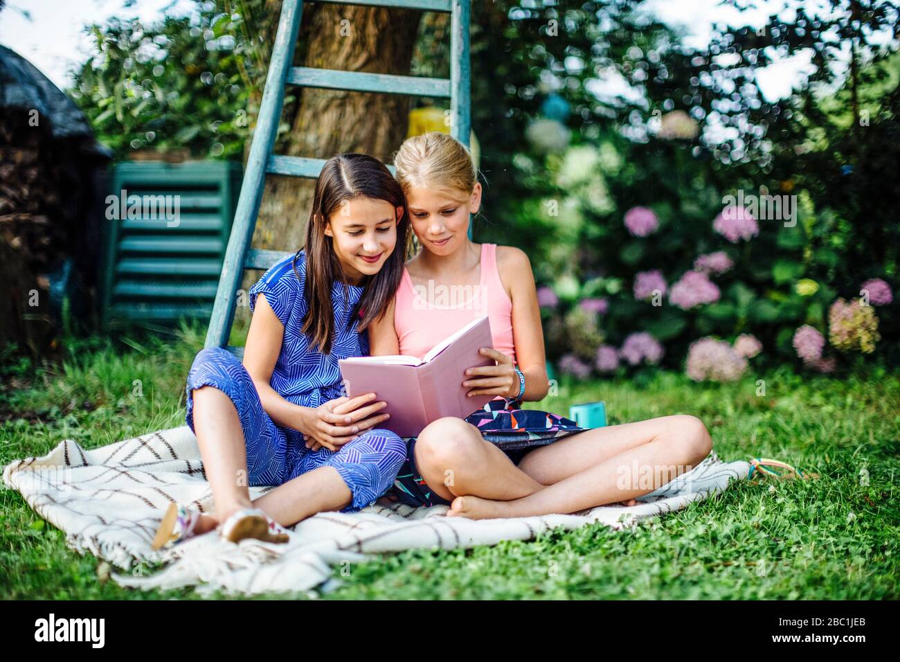 Smiling girls reading a book in garden together Stock Photo