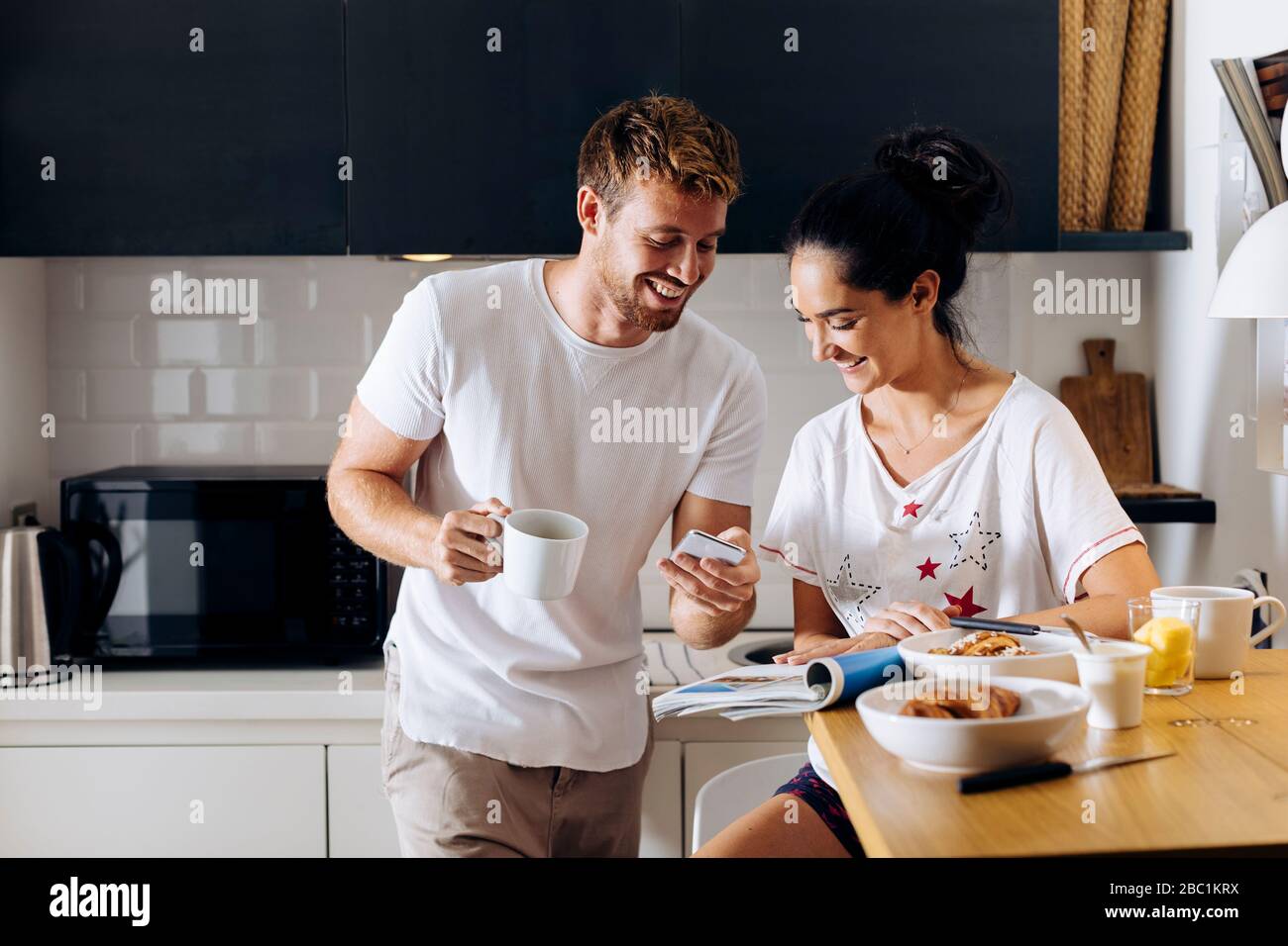 Happy young couple in the kitchen looking at cell phone Stock Photo