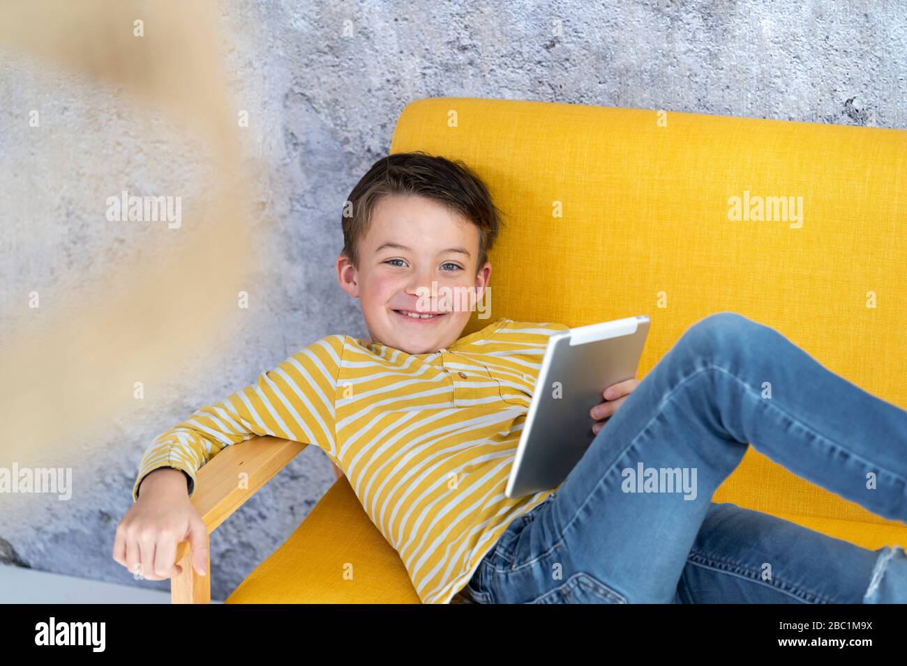 Boy playing with tablet on yellow couch Stock Photo