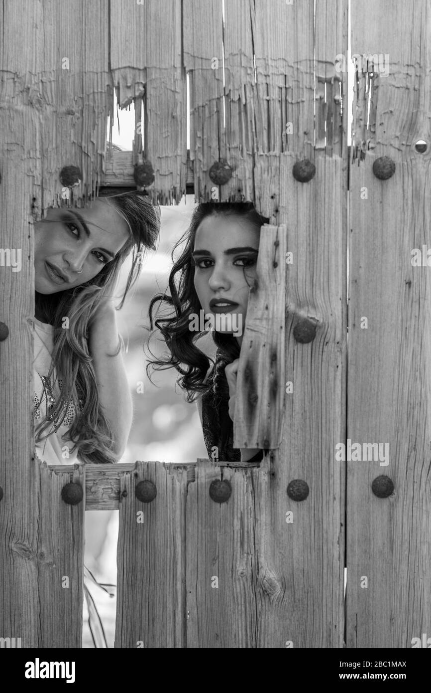 Portrait of two young women behind wooden fence looking through hole Stock Photo