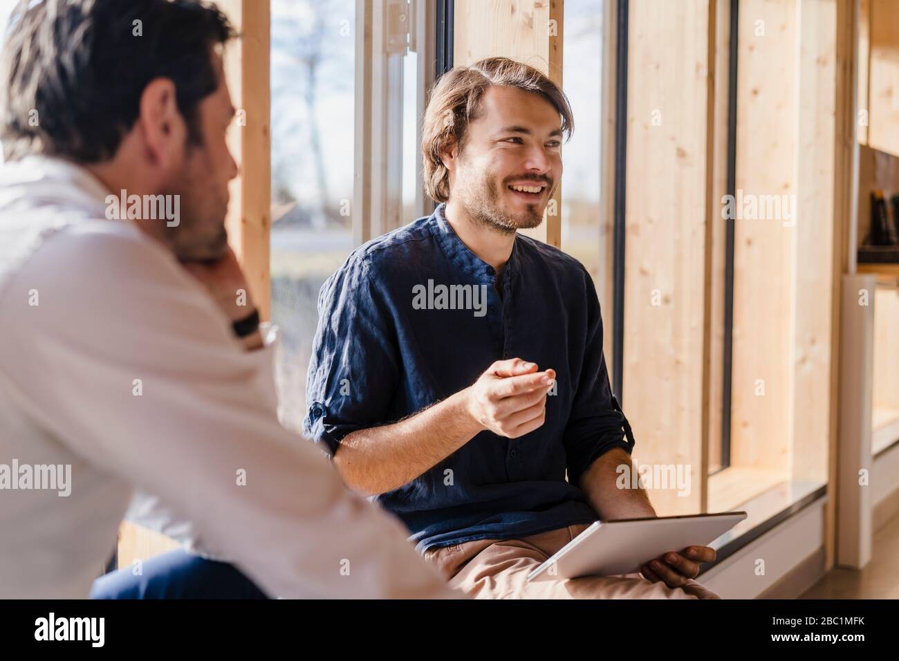 Two businessmen with tablet talking at the window in open-plan office ...