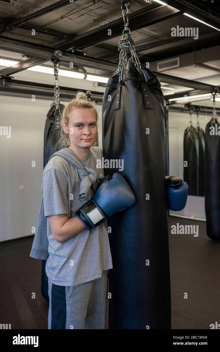 Portrait of woman with boxing gloves at sandbag in gym Stock Photo