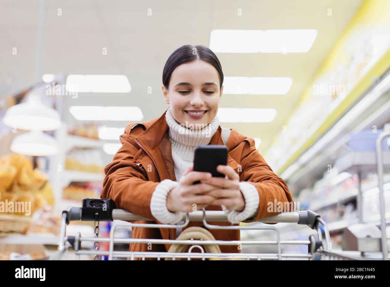 Woman with smart phone pushing shopping cart in supermarket Stock Photo ...