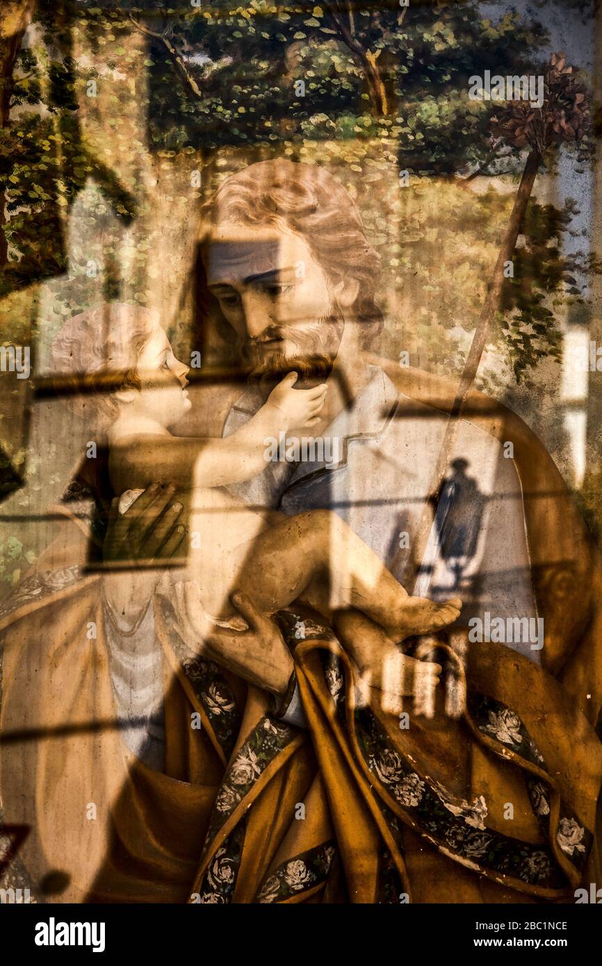 Reflections on a glass panel in front of a figure of Jesus carried by his father. Stock Photo