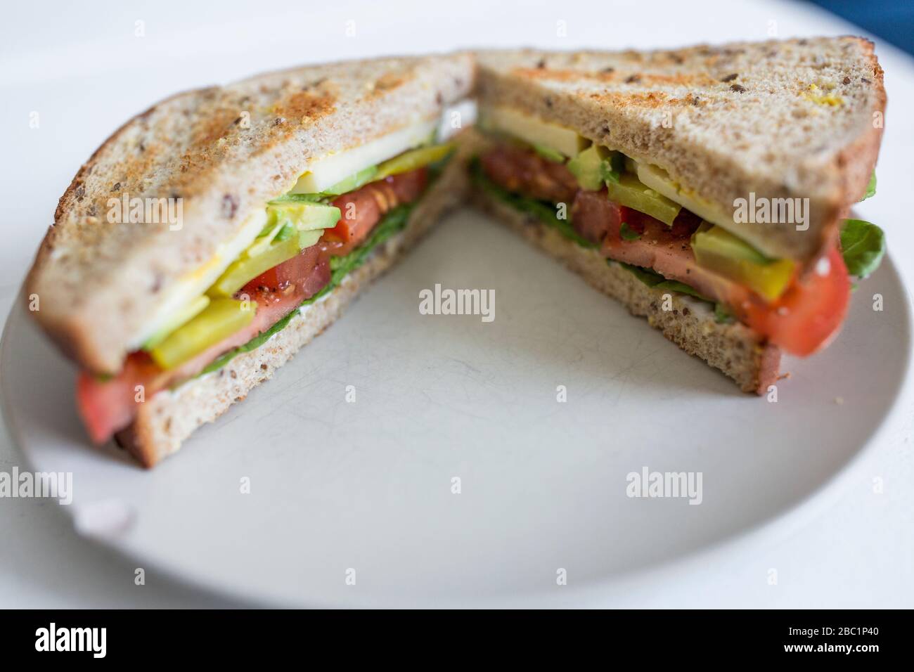 A vegetarian sandwich with avocado and tomato on whole wheat bread ready for a healthy, delicious lunch. Stock Photo