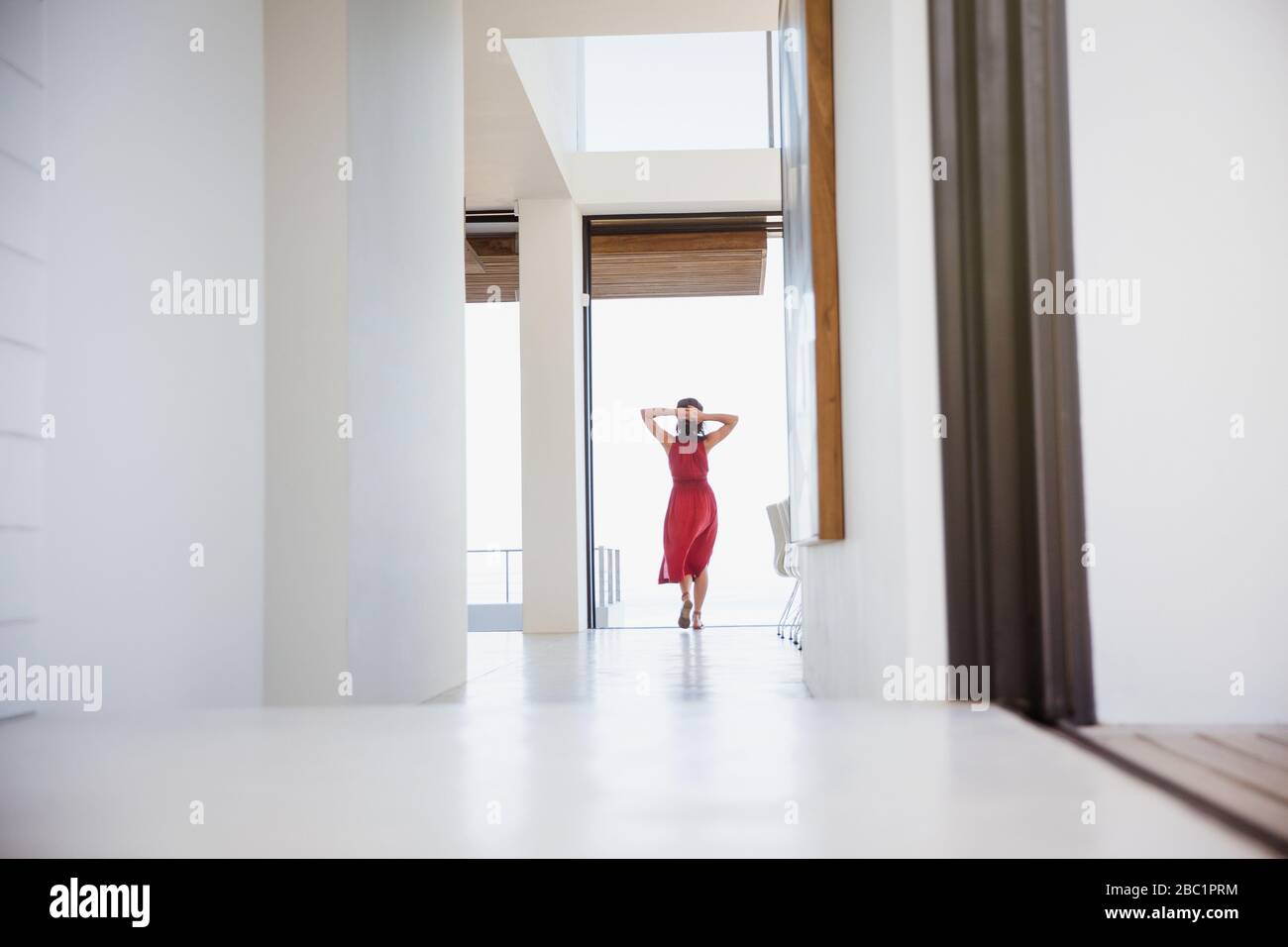 Woman standing with hands behind head in home corridor Stock Photo