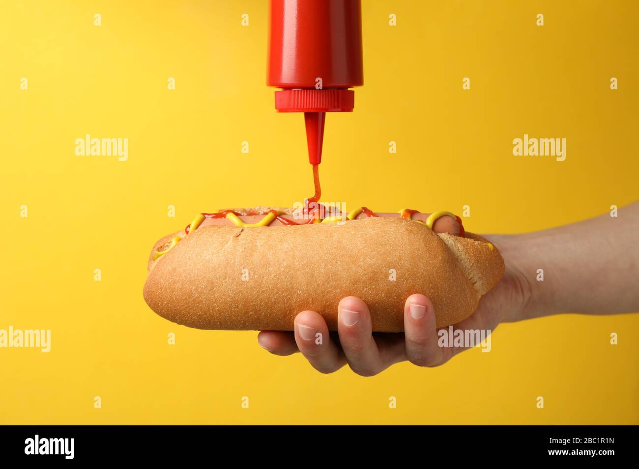 Person pouring ketchup on hot dog, on yellow background Stock Photo Alamy