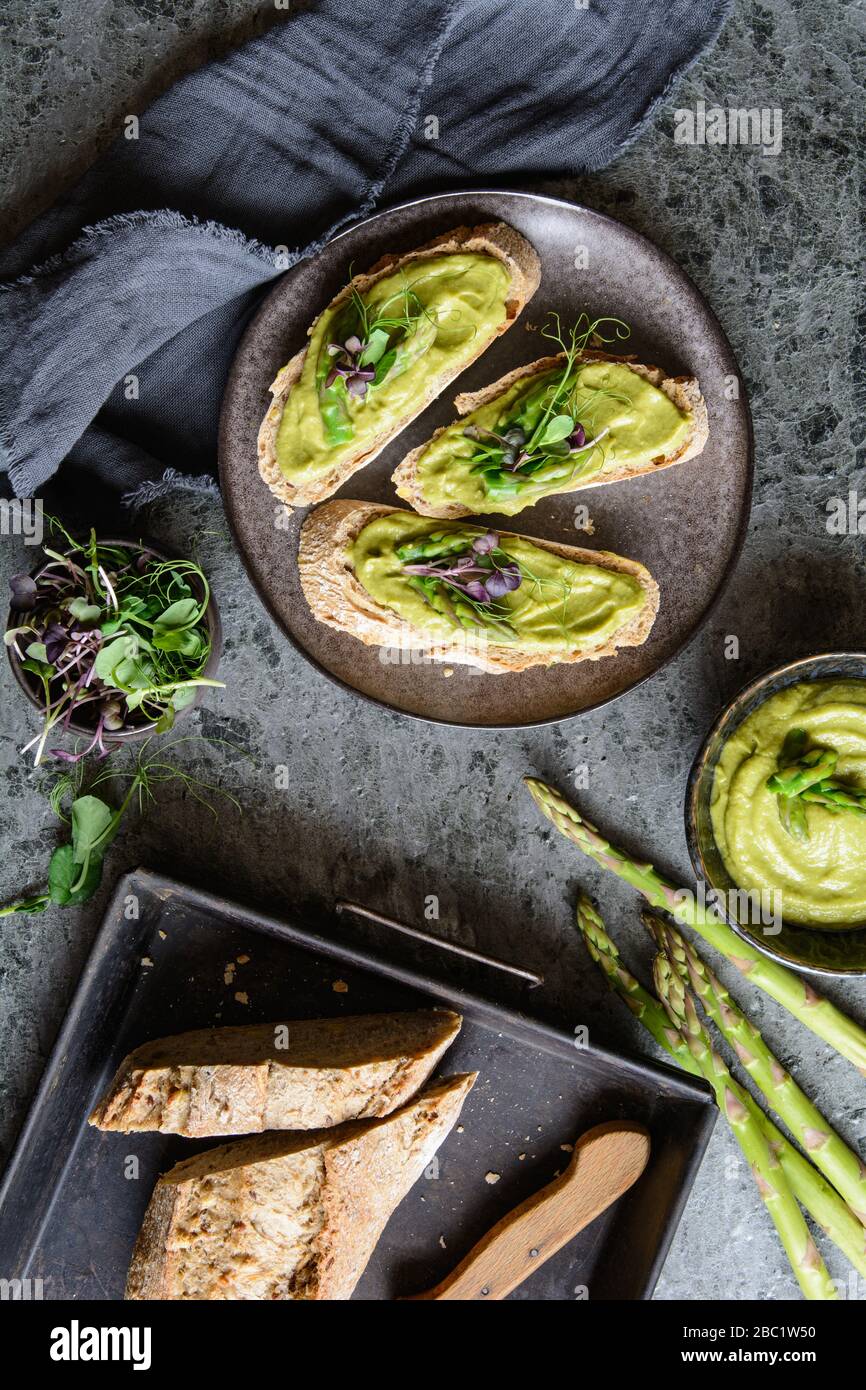 Slices of bread with vegetarian avocado, zucchini and asparagus spread, topped with pea and radish sprouts on a ceramic plate Stock Photo