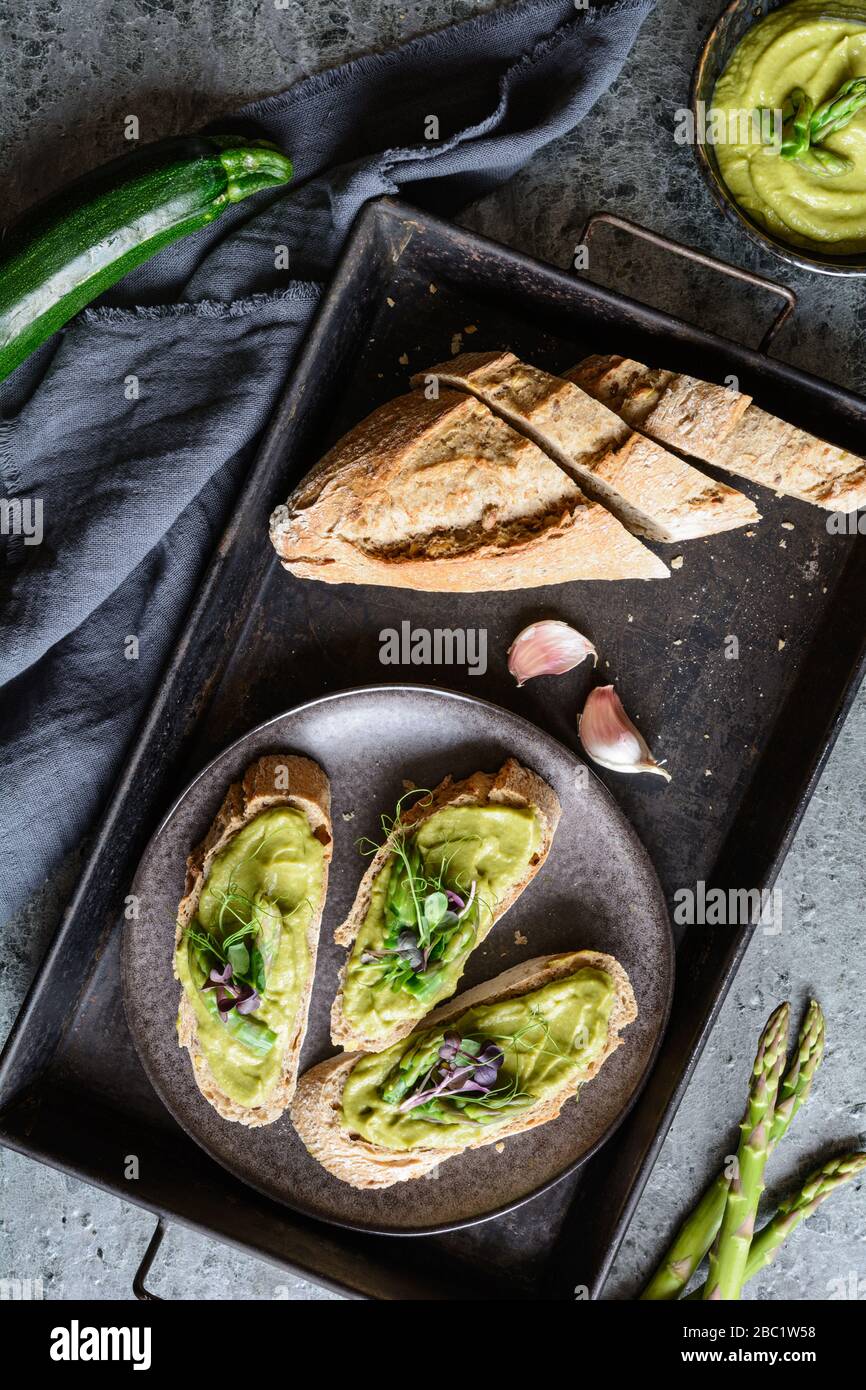Slices of bread with vegetarian avocado, zucchini and asparagus spread, topped with pea and radish sprouts on a ceramic plate Stock Photo