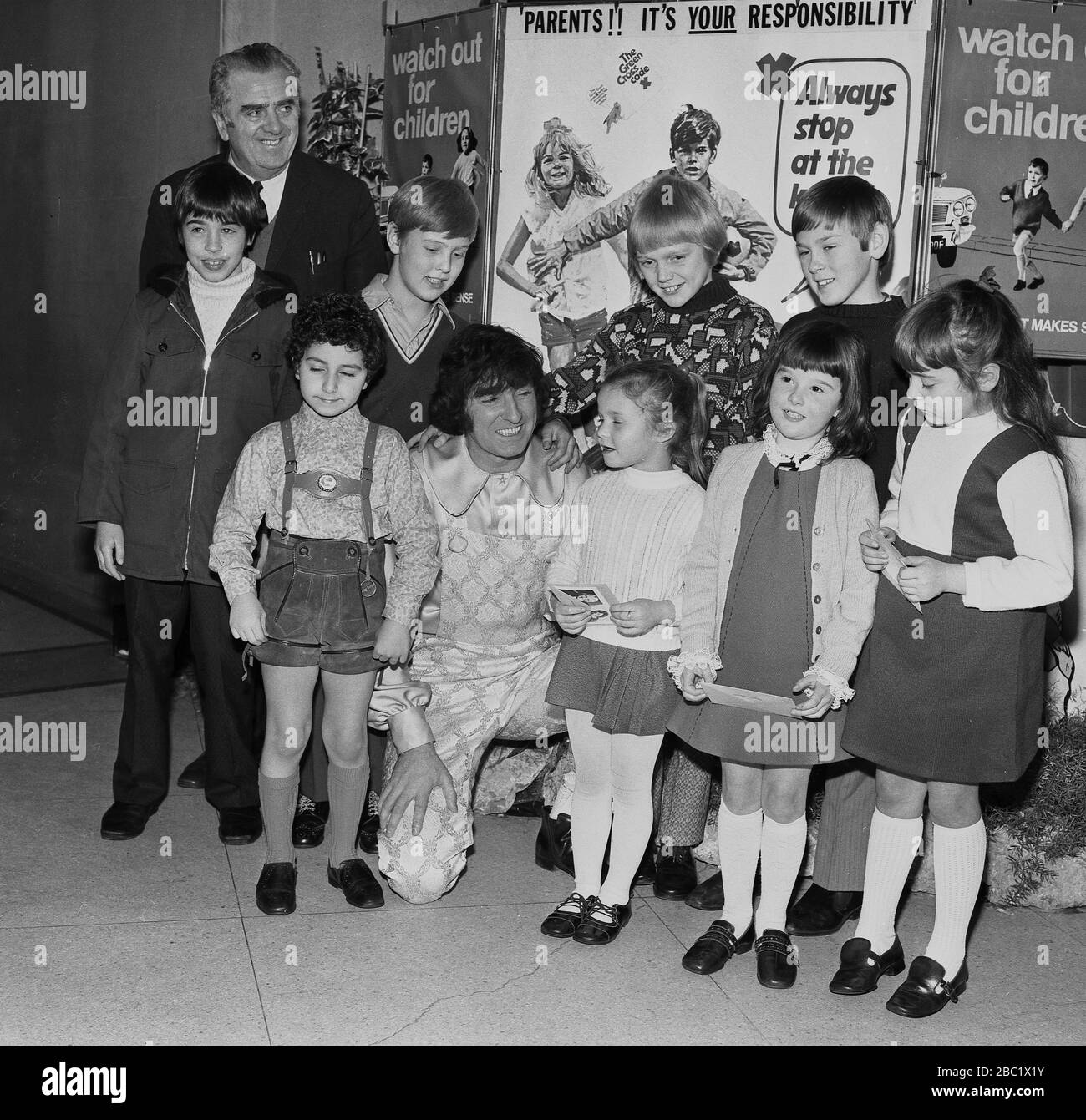 1970s, British comedian and childrens entertainer, Ken Goodwin, with a group of primary schoolgirls and boys infront of promotional posters for children road safety, and the Green Cross Code in the Borough of Lewisham, South East London, England, UK. Stock Photo