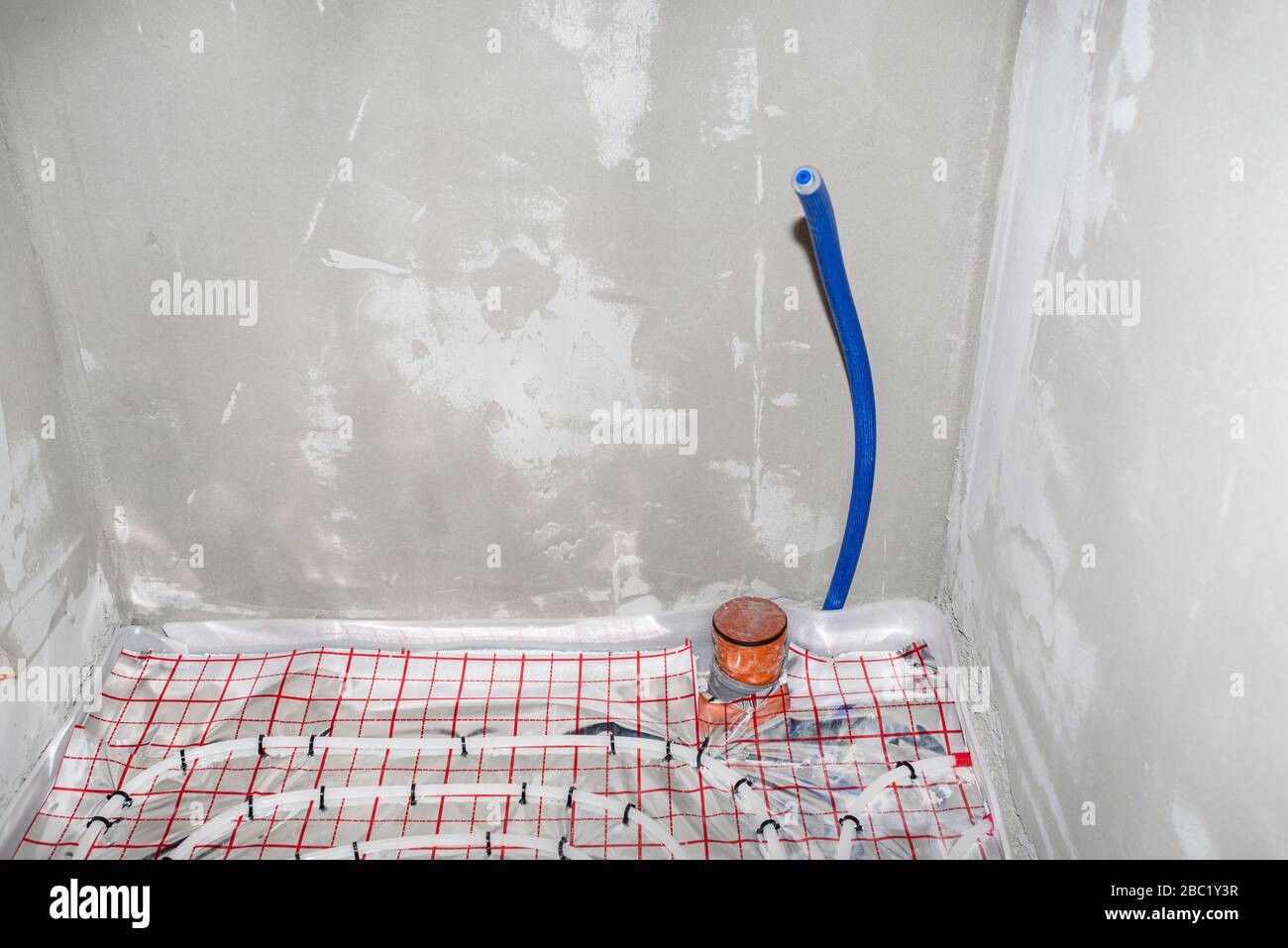 Blue plastic pipe with cold water coming out of the floor, water connection to the toilet cistern. Visible drains in the bathroom. Stock Photo
