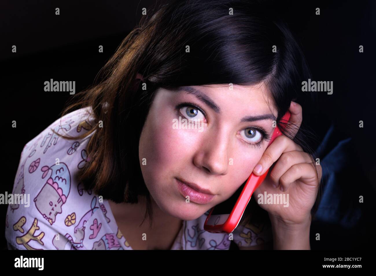 cute young woman with black hair and green eyes talking on a cell phone in a red case Stock Photo