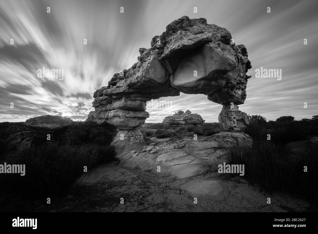A dramatic black and white landscape photograph of an incredible rock arch before sunrise, with fast moving clouds against a moody sky, taken in the C Stock Photo