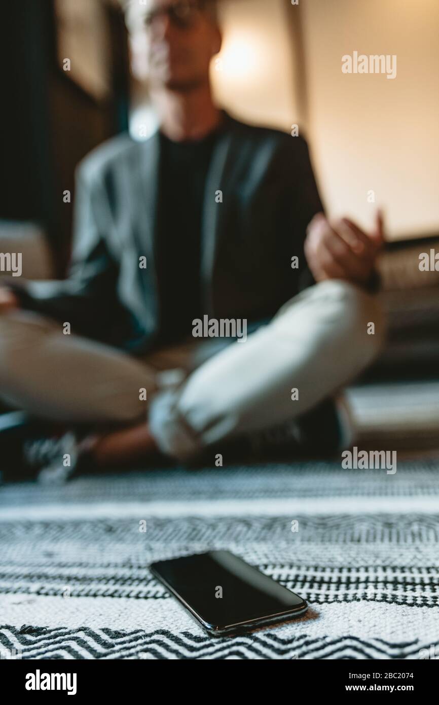Low angle shot of a mid adult businessman doing yoga meditation with his mobile phone in front. business professional meditating in yoga pose in offic Stock Photo