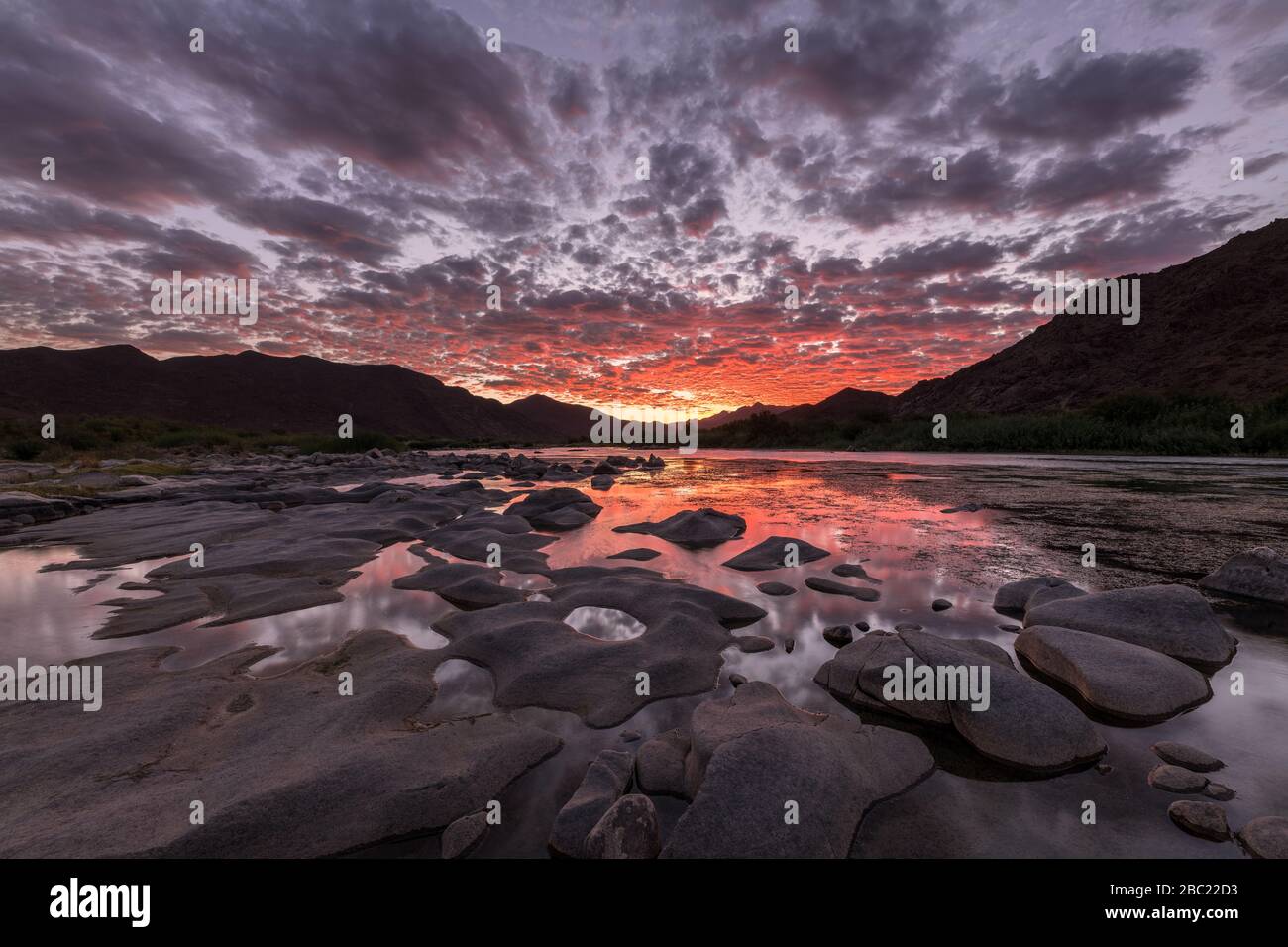 A beautiful landscape after sunset with mountains and the Orange River, with dramatic red clouds reflecting in the water’s surface, taken in the Richt Stock Photo