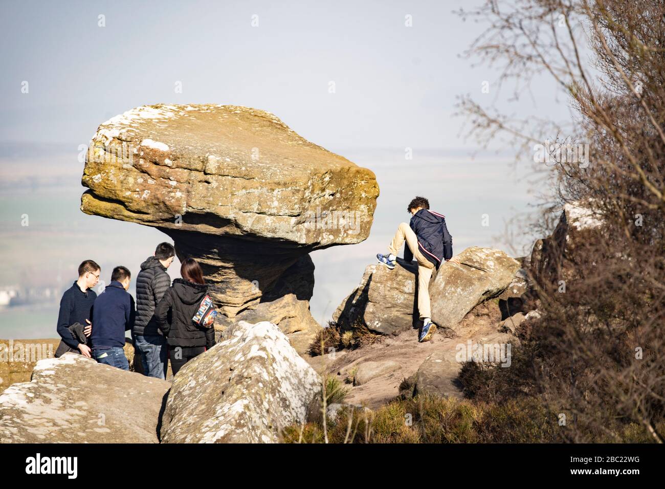 Group of tourists stood next to 'The Druids Writing Desk' gritstone rock formation, Brimham Rocks, Harrogate, North Yorkshire, England, UK. Stock Photo