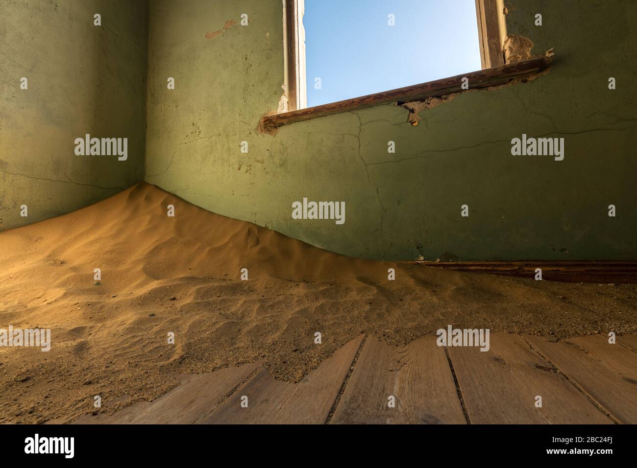 A close up photograph of an old, broken window, with desert sand piling in the corner of an abandoned house, taken in the ghost town of Kolmanskop, Na Stock Photo