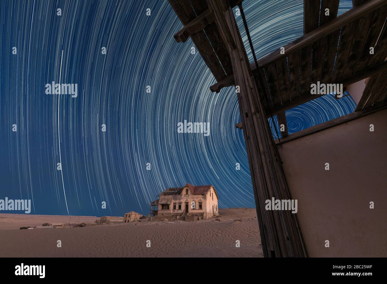 A beautiful night sky photograph with circular star trails against a deep blue sky, with an abandoned house and desert sand in the background, taken i Stock Photo