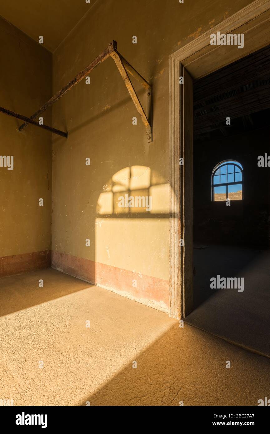 A vertical photograph inside an abandoned house with an open doorway leading into another room and a shaft of golden light streaming in the room, take Stock Photo