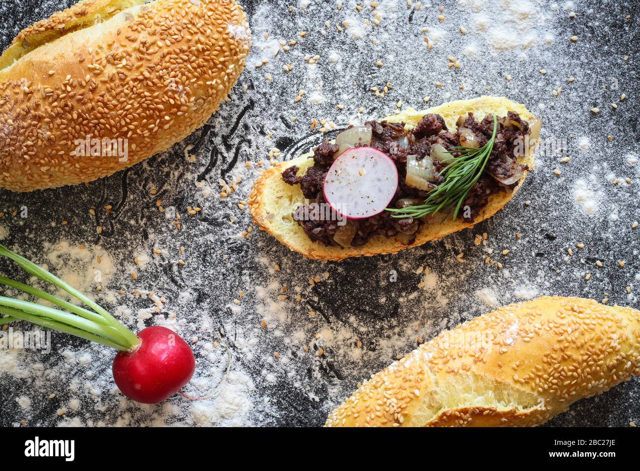 Corn bread roll with warm kaszanka (polish blood sausage) stewed with onion on black background sprinkled with flour Stock Photo