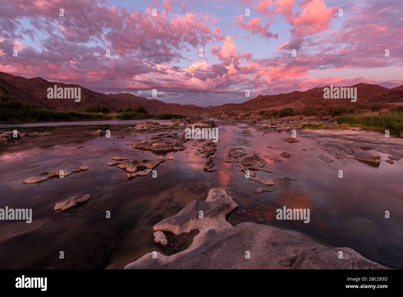 A beautiful landscape taken after sunset with mountains and the Orange River, with dramatic pink clouds reflecting in the water’s surface, taken in th Stock Photo