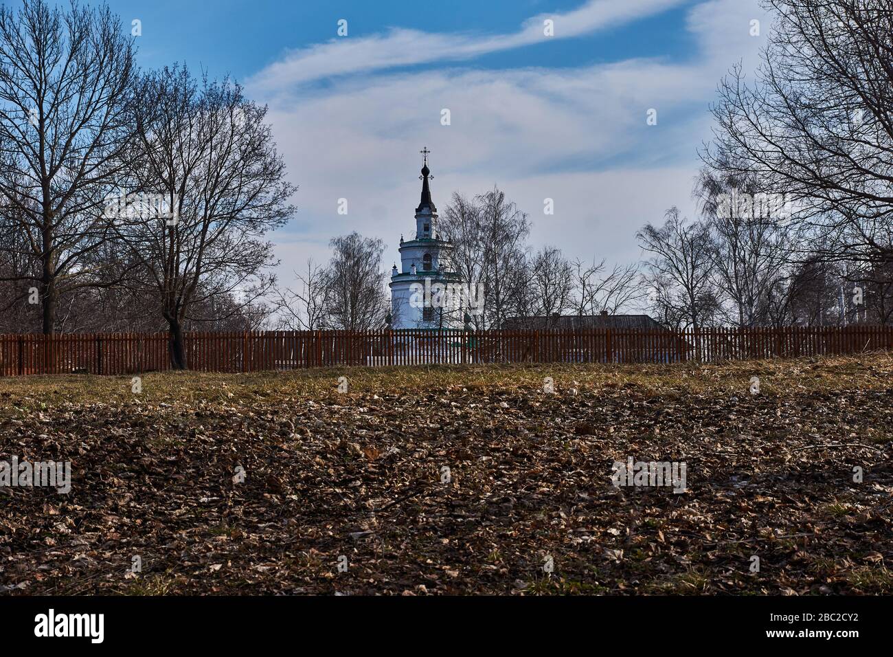 Ancient orthodox temple among trees. Landscape of central Russia. Windows, roof and doors are visible through branches. The village of Big Boldino. Stock Photo