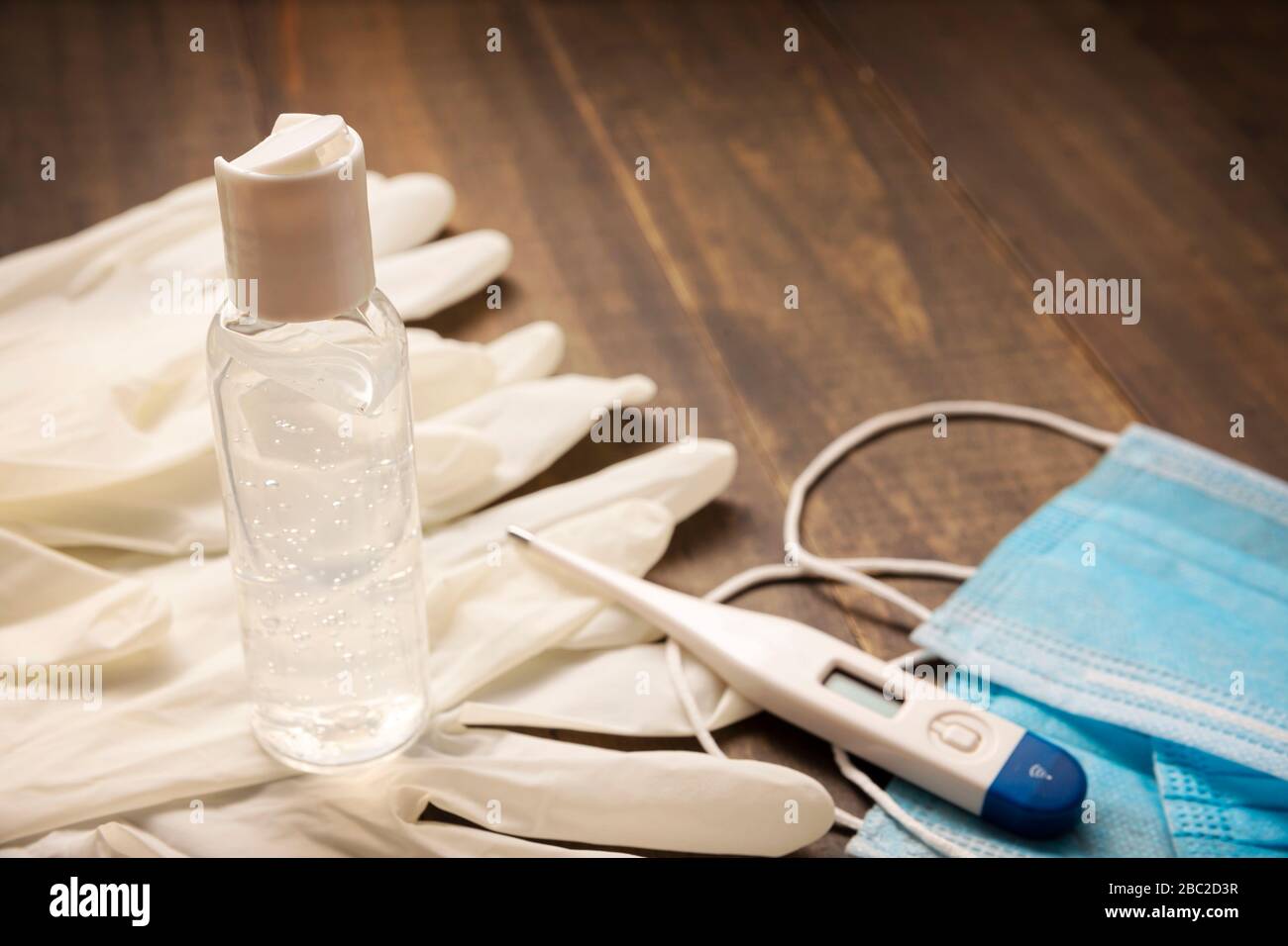 medical latex gloves, protective masks,thermometer and hand sanitizer gel bottle for protection on wooden background. Useful for pandemic prevention c Stock Photo