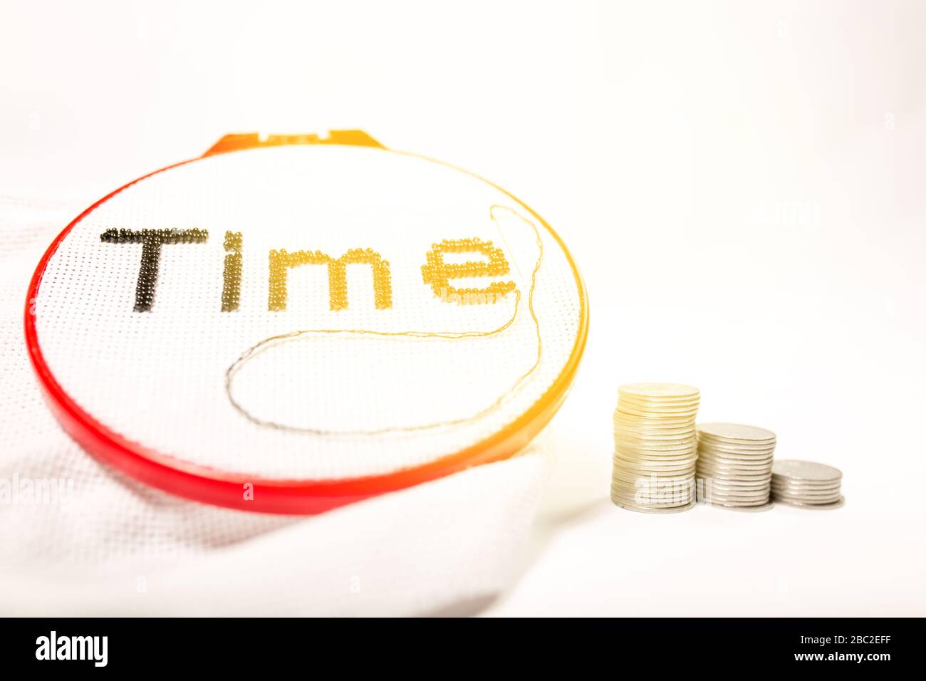 The concept of the value of time spent. The word time is embroidered in black beads on a white background with a stack of coins on a white background. Stock Photo