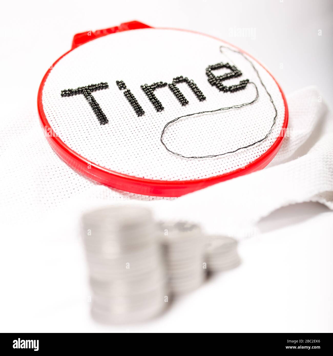 The word time is embroidered in black beads on a white background with a stack of coins on a white background. Stock Photo