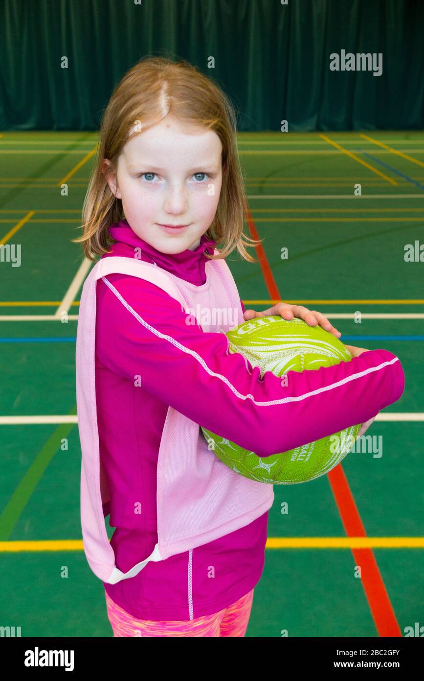 10 Year old girl holds / hold / holding a netball on the court at the end of an indoor / inside netball lesson / game. (116) Stock Photo