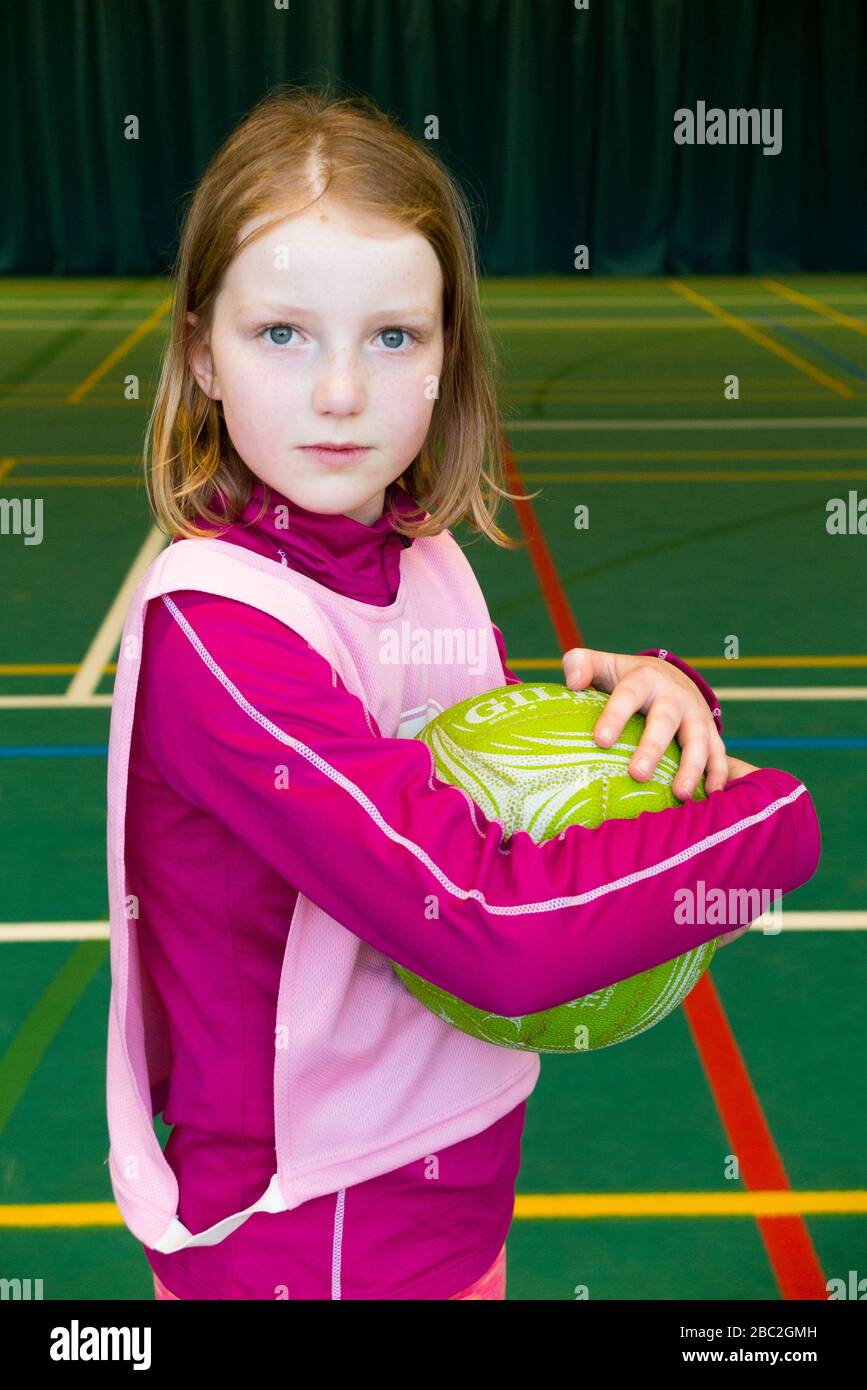 10 Year old girl holds / hold / holding a netball on the court at the end of an indoor / inside netball lesson / game. (116) Stock Photo