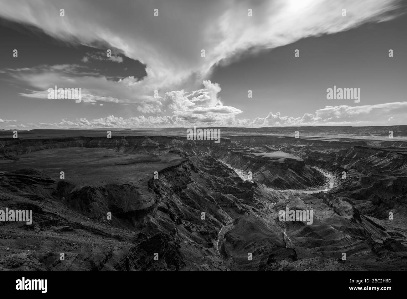 A black and white landscape taken at sunset on a stormy day on top of the arid and stark Fish River Canyon, Namibia, with the gorge and river in the f Stock Photo
