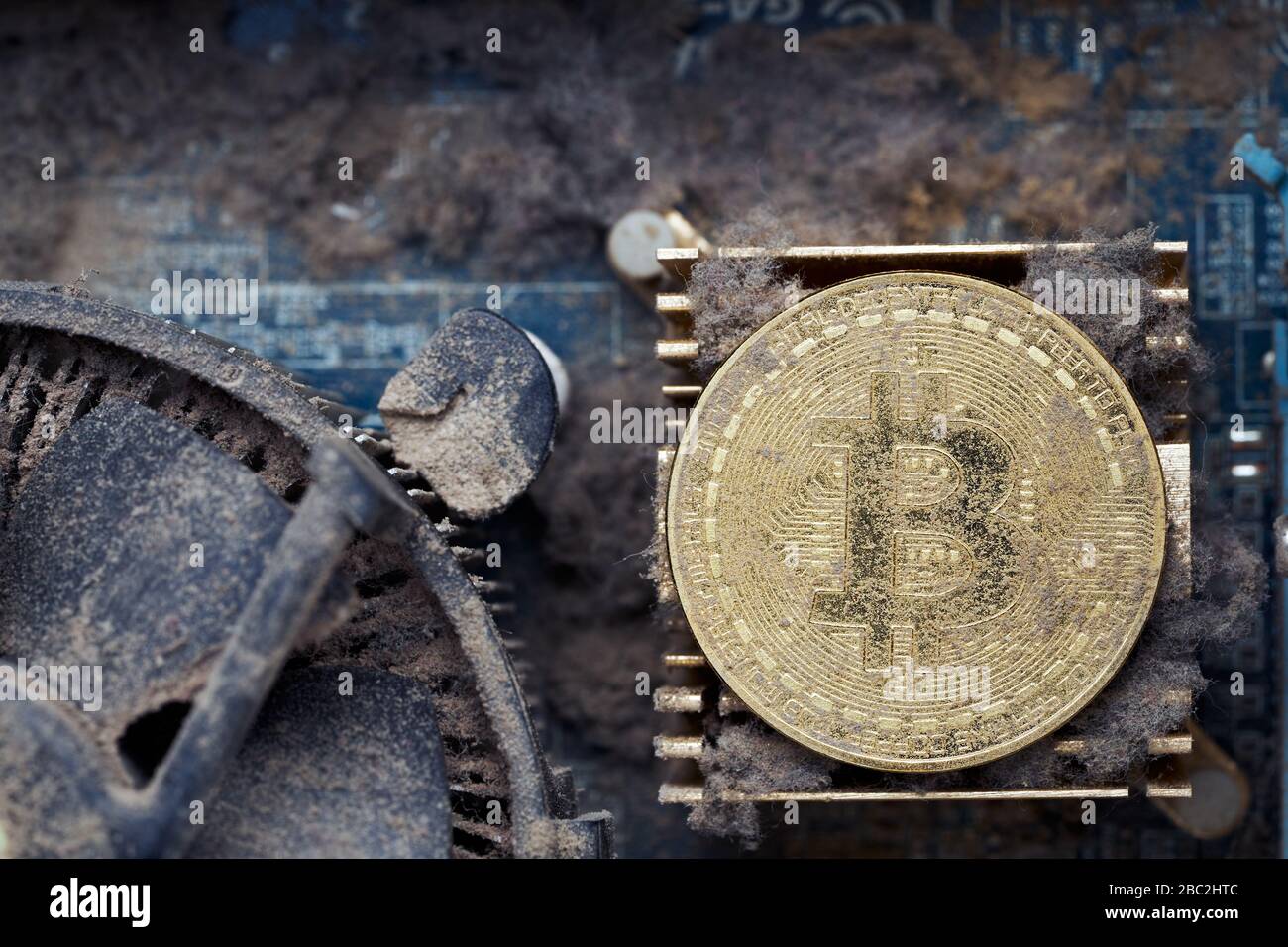 Dirty golden bitcoin inside an old broken computer covered with dust Stock Photo