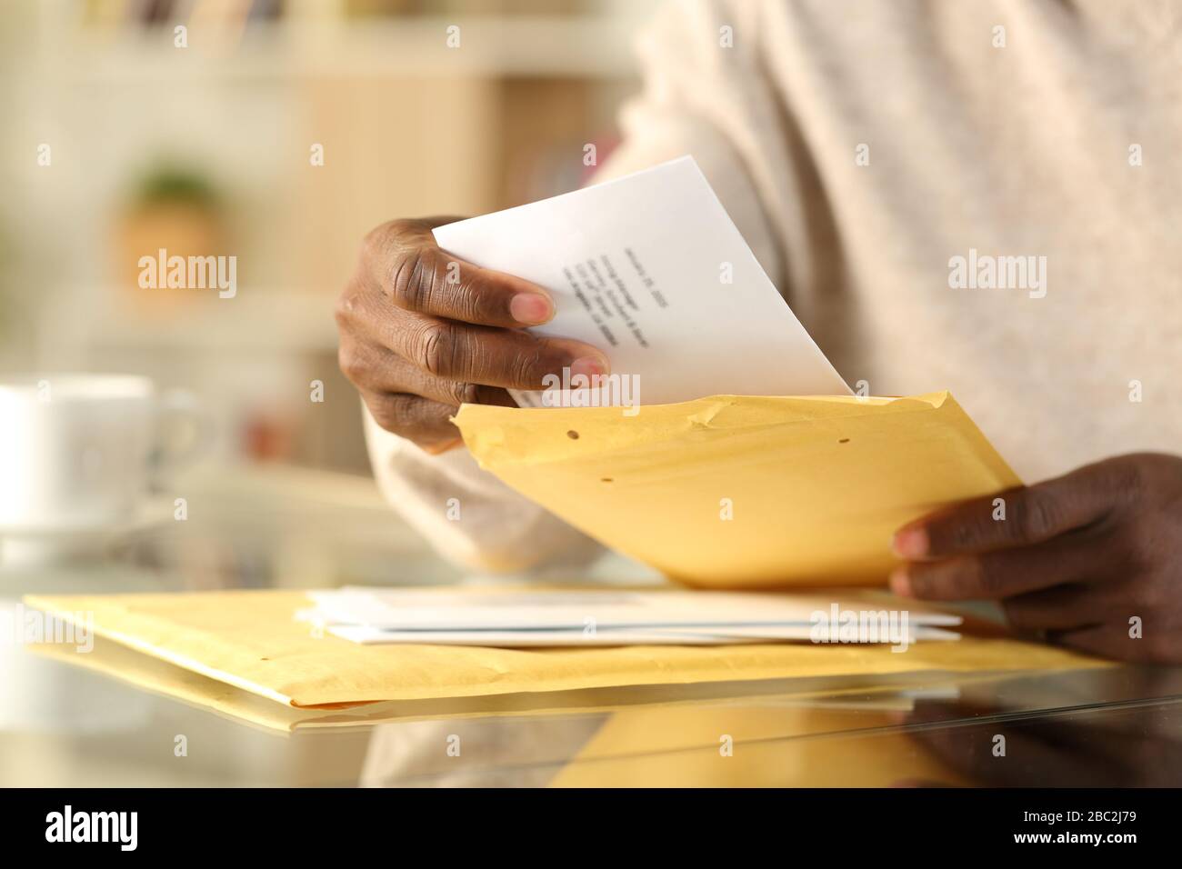Close up of black man hands opening a padded envelope with letter on a desk at home Stock Photo