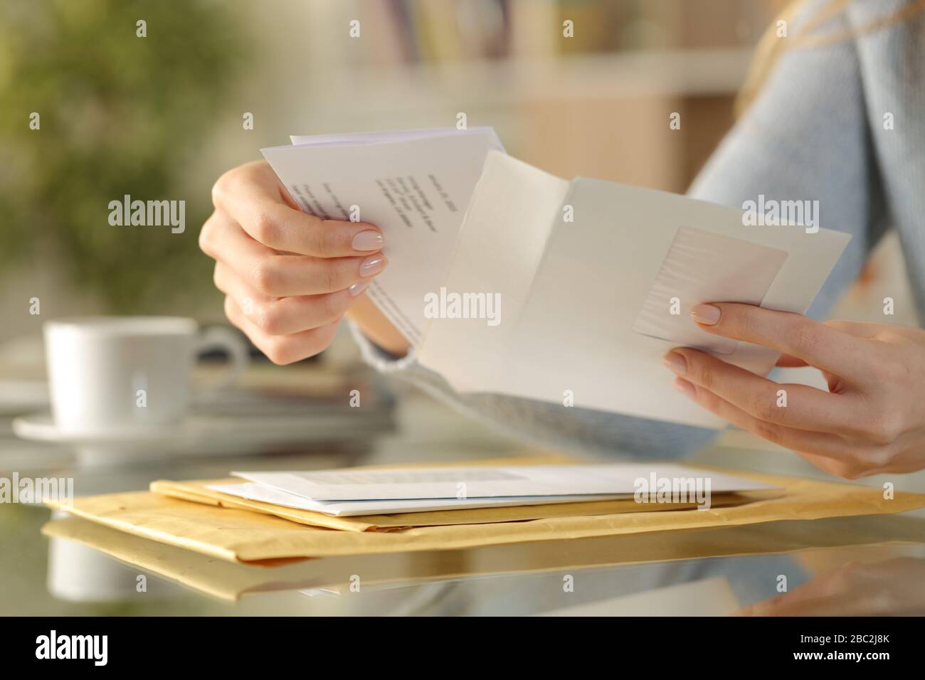 Close up of girl hands opening an envelope with a letter inside on a desk at home Stock Photo