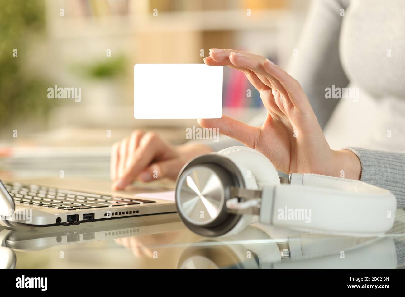 Close up of woman hand buying music online with blank credit card on laptop with headphones on a desk at home Stock Photo