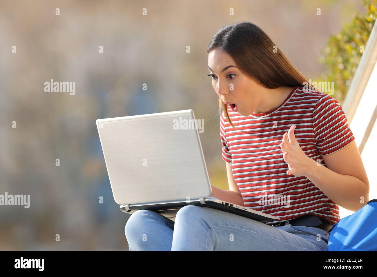 Amazed student checking surprising news on laptop sitting in a campus Stock Photo