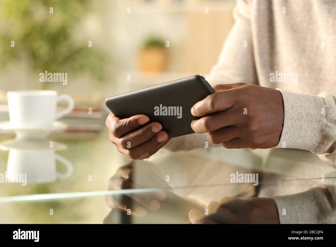 Close up of black man hands playing video game on smartphone sitting on a desk at home Stock Photo