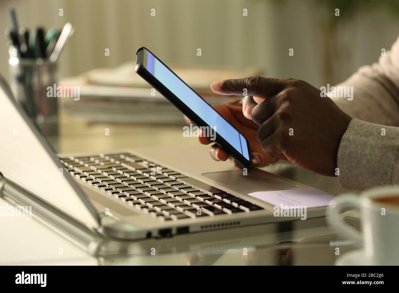 Close up of black man hands using smart phone with laptop on a desk at home Stock Photo
