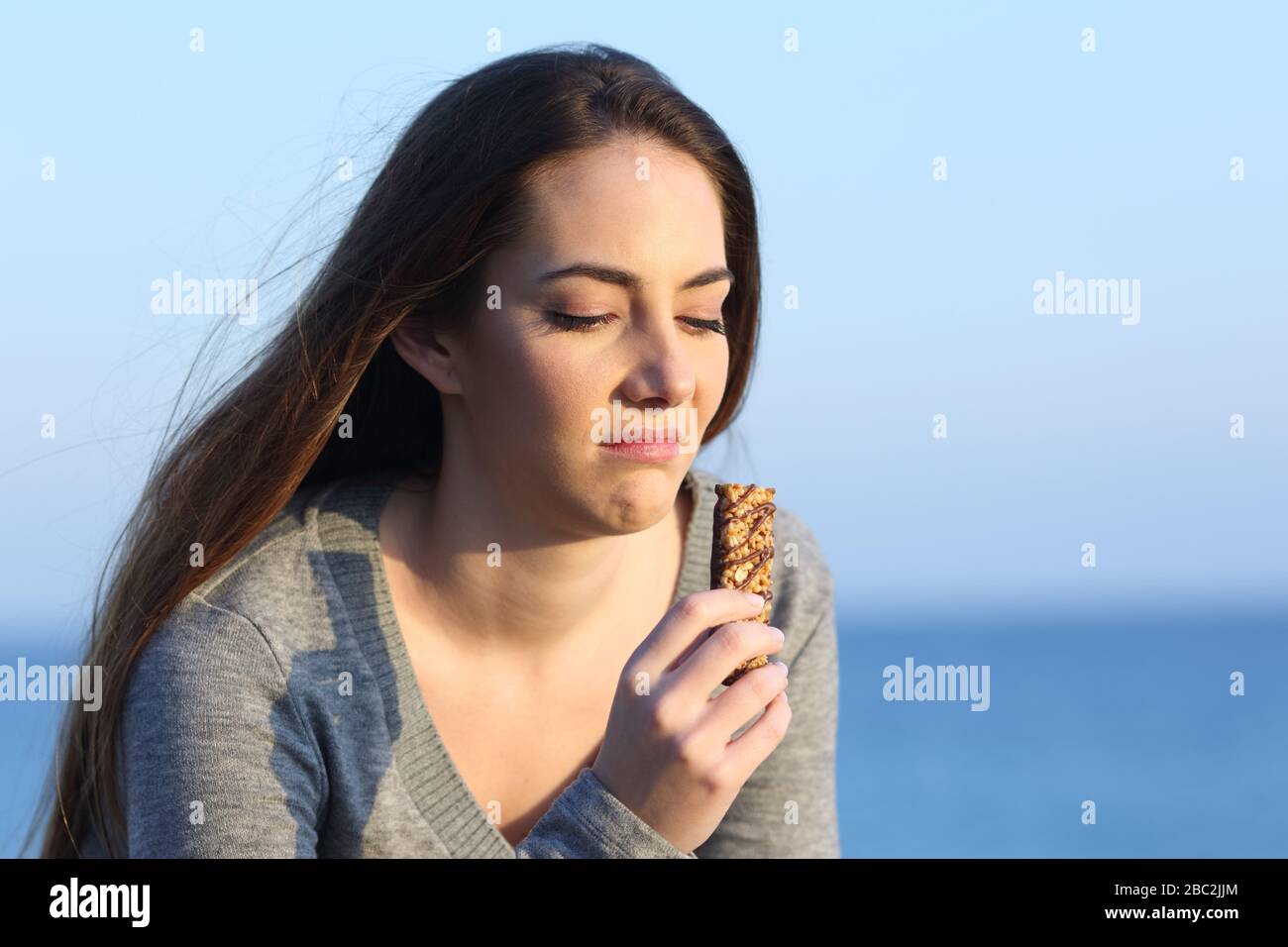 Disgusted woman tasting a bad energy bar on the beach Stock Photo Alamy
