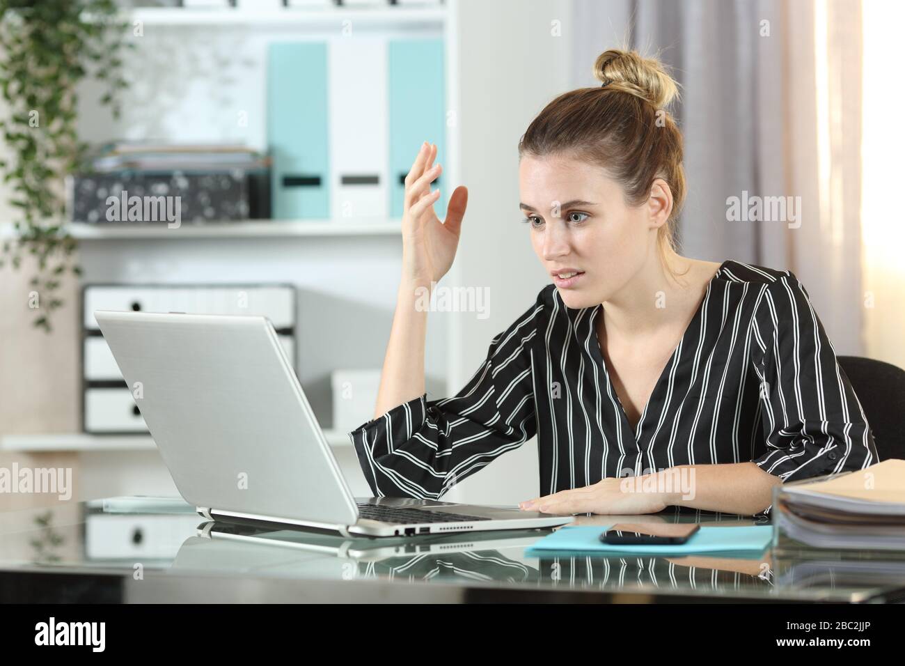 Frustrated entrepreneur woman with laptop complaining sitting on a desk in the office Stock Photo